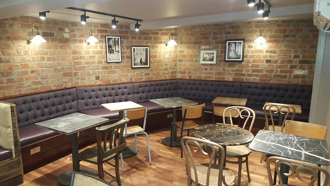 tables and chairs with a long sofa laid out in a refurbished cafe