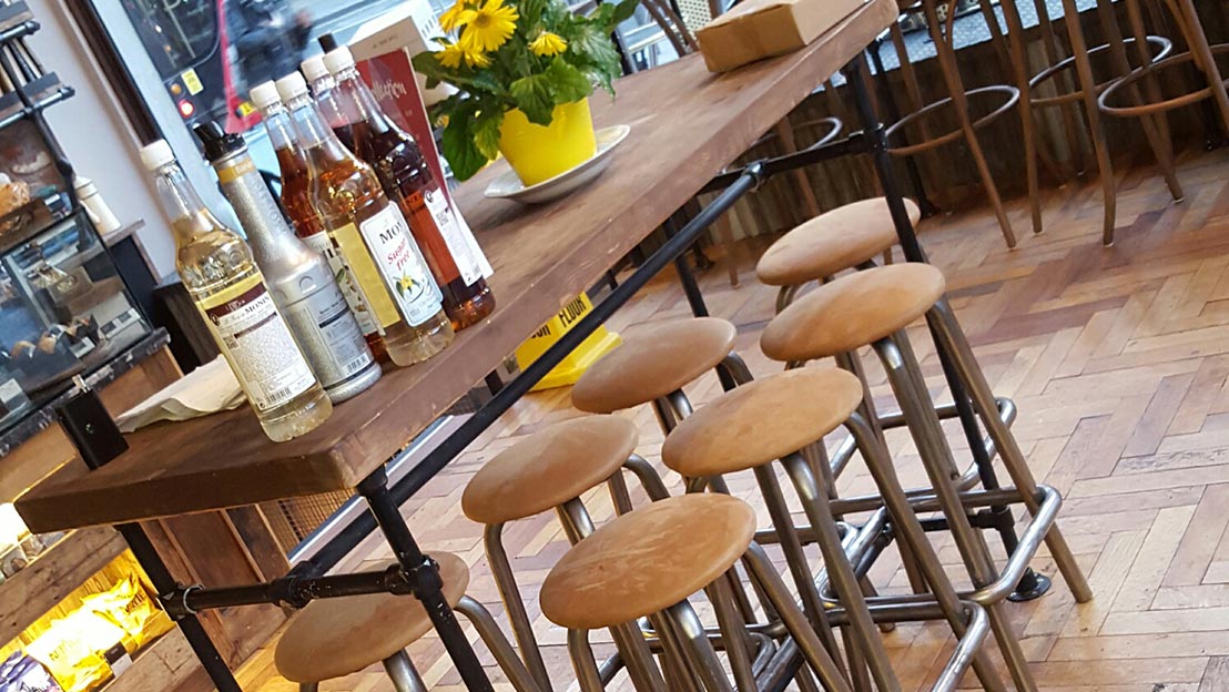 A high table with coffee syrups on with high stools in a refurbished cafe.